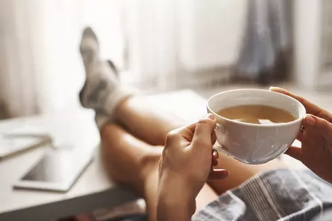 frau-sitzt-auf-sofa-mit-teetasse-in-den-händen-gesundheit-gaspan-bauchschmerzen-voellegefuehl-vorbeugen