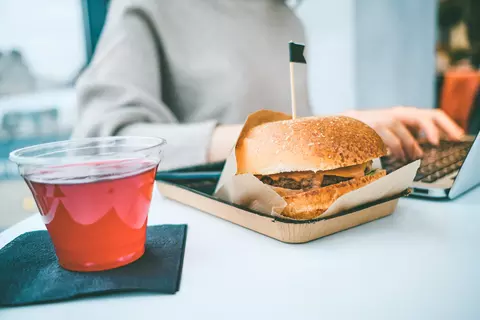 personne-assise-devant-laptop-et-travaille-à-côté-burger-et-courte-alimentation-saine-stress-digestion