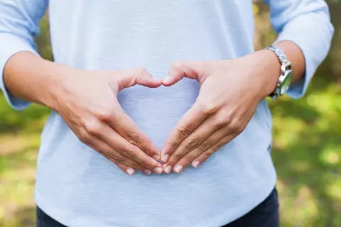 Frau formt mit den Händen ein Herz vor dem Bauch – Symbol für Bauchwohl und Verdauung