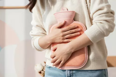 Frau hält eine Wärmeflasche an den Bauch, um Blähungsbeschwerden zu lindern.