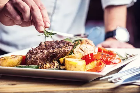 Mann kocht Abendessen und garniert mit Kräutern.