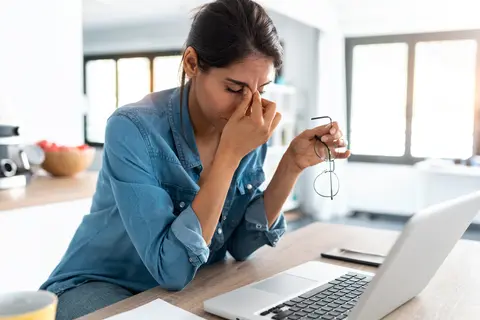 Junge Frau am Laptop greift sich an den Kopf - Reizdarmsyndrom Auslöser Stress