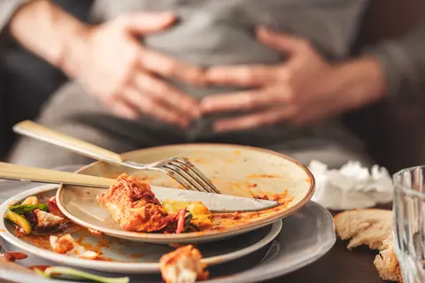 Person sitzt vor leeren Tellern und hält sich den Bauch - Reizdarmsyndrom Auslöser Ernährung