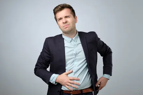 Mann hält sich den Bauch und wirkt angespannt – Blähbauch mit Bauchkrämpfen und Beschwerden