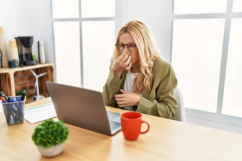 Frau im Büro hält sich die Nase zu – unangenehmer Geruch als Thema bei Flatulenzen.
