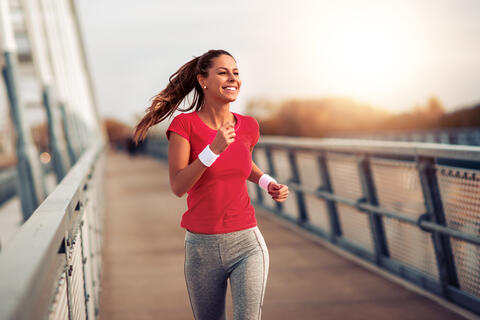 Junge Frau joggt über eine Brücke – Bewegung kann Stress reduzieren und das Wohlbefinden des Bauchs unterstützen.