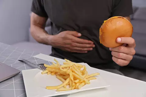 homme-au-t-shirt-noir-tenant-dans-une-main-un-burger-et-l'autre-main-devant-le-ventre-frites-sur-une-assiette-sensation-de-plomb-flatulences