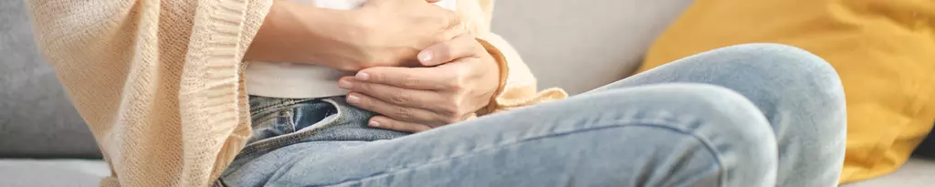 frau-sitzt-mit-bauchschmerzen-auf-dem-sofa-hält-sich-hände-auf-den-bauch-bauchschmerzen-voellegefuehl-magenbrennen-gaspan