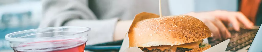 person-sitzt-vor-dem-laptop-und-arbeitet-daneben-burger-und-eistee-gesundes-essen-stress-verdauung